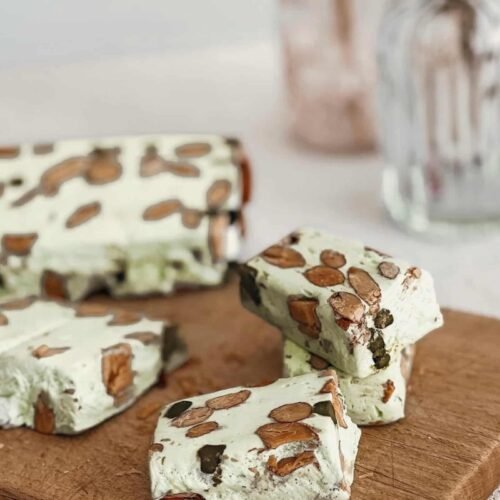 Cubes de nougat blanc tendre à la pistache et crème de pistache sur une planche en bois