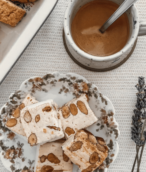 Nougat blanc aux amandes servi avec un café chaud et des croquants artisanaux sur une table décorée de lavande.
