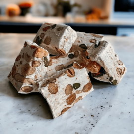 Gros plan sur des tranches de nougat royal artisanal, riche en amandes, noisettes et pistaches entières, révélant une texture moelleuse.